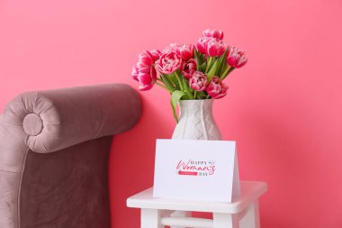 Laleli vazo ve renkli duvarın yanındaki masada mutlu kadınlar günü yazılı tebrik kartı.