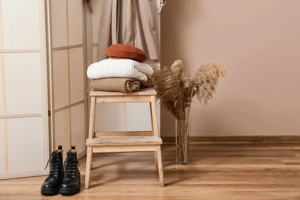 Step stool with stack of warm clothes, boots and vase in hall