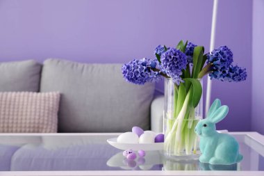Sümbül çiçekli vazo, kanepenin yanındaki masada paskalya tavşanı ve yumurta.