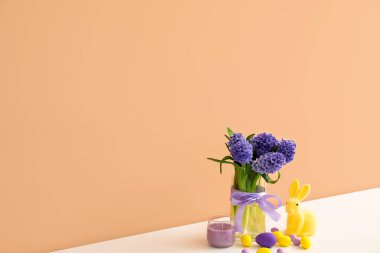 Sümbül çiçekli vazo, Paskalya yumurtası, tavşancık ve renkli duvara yakın mum.