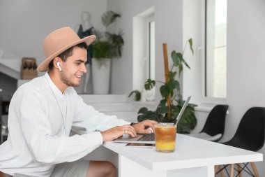 Kafedeki masada dizüstü bilgisayar kullanan kulaklıklı genç bir adam.