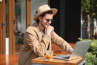 Sokak kafesindeki masada dizüstü bilgisayar kullanan şık bir genç.