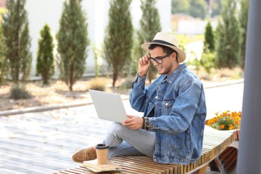 Bilgisayarlı yakışıklı adam parkta bankta oturuyor.