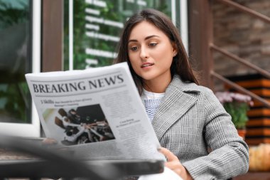 Caddedeki kafede gazete okuyan güzel genç bir kadın.