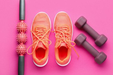 Pembe arka planda şık halterler, ayakkabılar ve masaj rulosu.