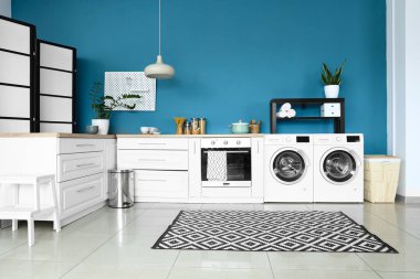 Modern çamaşır makineleri, fırın ve beyaz tezgahları olan şık bir mutfak.