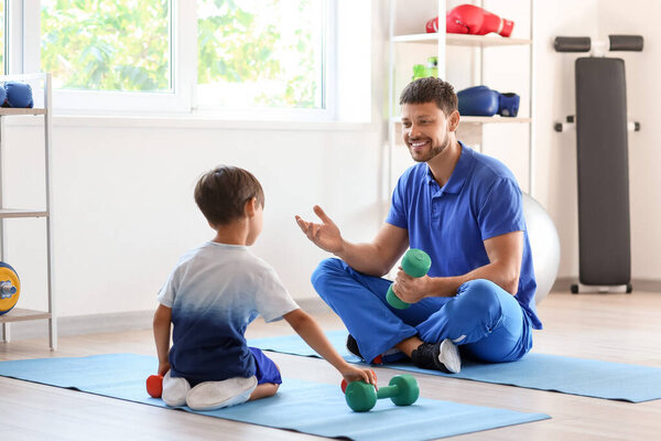 Тренер мужского пола с гантелями и маленьким мальчиком в спортзале