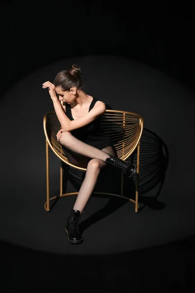 穿着黑色紧身衣坐在深色背景扶手椅上的时髦年轻女子 — 图库照片