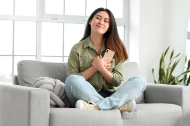 Evdeki kanepede oturan erkek arkadaşından gelen mesajı okuduktan sonra mutlu bir Asyalı kadın.