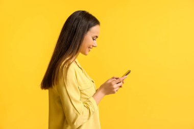 Sarı arka planda cep telefonu olan güzel bir genç kadın.