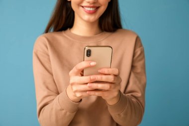 Mavi arka planda cep telefonu olan güzel genç bayan, yakın plan.