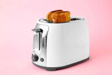 Pembe arka planda ekmek dilimleri olan modern bir tost makinesi.