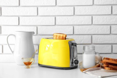 Ekmek dilimli modern tost makinesi, mason süt ve bal kavanozu ışık masasında.