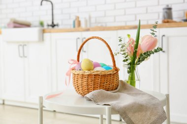 Mutfaktaki masada boyanmış Paskalya yumurtaları ve çiçeklerle hediye sepeti.