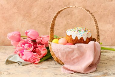 Paskalya yumurtaları boyalı hediye sepeti, lale çiçekleri ve bej arka planda pasta.