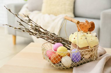 Gift basket with painted Easter eggs, pussy willow branches and cake on table in room