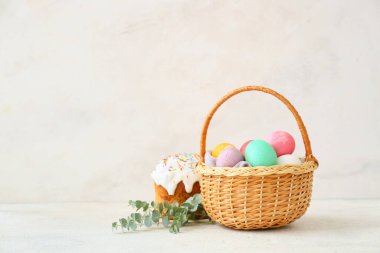 Renkli Paskalya yumurtaları ve açık arkaplanda pastayla hediye sepeti.