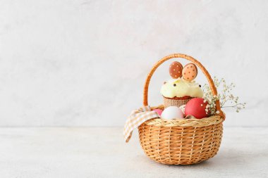 Renkli Paskalya yumurtaları, çiçekler ve açık arkaplanda pasta olan hediye sepeti.