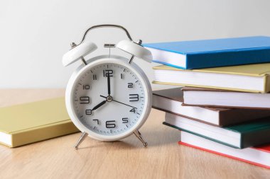 Masada yığınla kitap ve çalar saat var. Yakın plan.