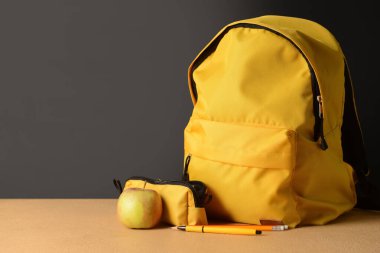 Sırt çantası, kalem kutusu ve elma koyu arka planda.