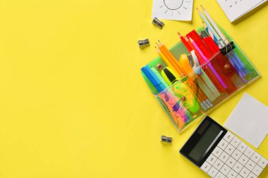 Sarı zemin üzerinde farklı kırtasiye ve hesap makinesi olan kalem kutusu