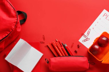 Kırmızı zemin üzerinde farklı kırtasiye malzemesi ve elma kompozisyonu