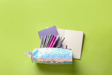 Yeşil zemin üzerinde kırtasiye malzemesi ve not defterleri olan kalem kutusu