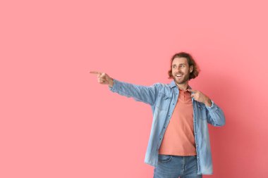 Pembe arka plandaki bir şeyi işaret eden şık elbiseli yakışıklı bir genç.