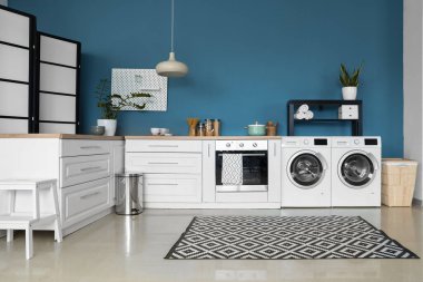 Modern çamaşır makineleri, fırın ve beyaz tezgahları olan şık bir mutfak.