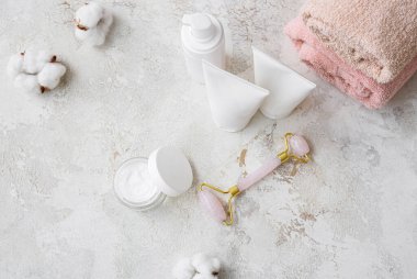 Kozmetik ürünleri, yüz masajı aracı ve arka planda pamuk çiçekleri