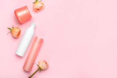 Pembe arka planda kozmetik ürünler ve gül çiçekleri.