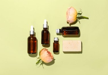 Yeşil zemin üzerinde kozmetik ürünler, sabun ve gül çiçekleri olan kompozisyon