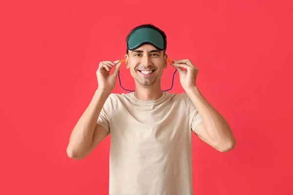 Smiling Young Man Sleeping Mask Putting Ear Plugs Red Background — Stock Photo, Image