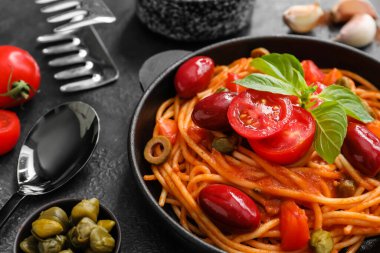 Lezzetli Puttanesca soslu kızartma tavası ve koyu arka planda malzemeler, yakın plan.