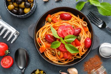 Lezzetli Puttanesca soslu tava ve koyu arkaplanda malzemeler.