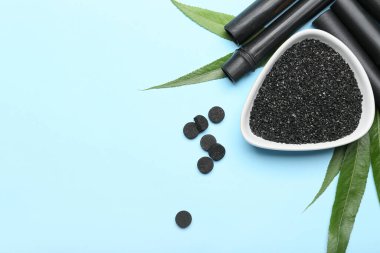 Etkinleştirilmiş karbon tozu, haplar, siyah bambu çubukları ve renk arkaplanındaki yapraklarla kompozisyon