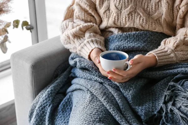 自宅でソファに座っておいしい青いお茶のカップを持つ女性 — ストック写真