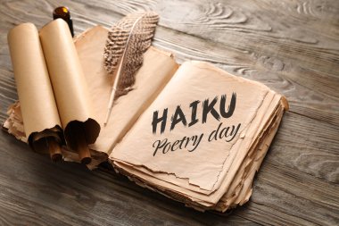 Open old book with text HAIKU POETRY DAY and feather with scrolls on wooden background clipart