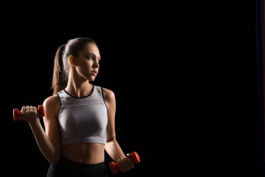 Siyah arka plan üzerine dumbbell ile sportif genç kadın