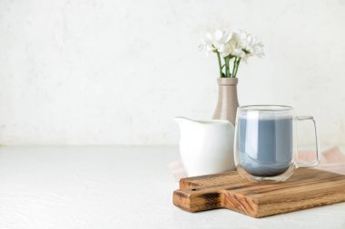 Ahşap tahta tahta tahta, cam bardak lezzetli kömür latte, çiçekli vazo ve hafif arka planda sütle sürahi.