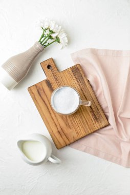 Ahşap tahta tahta tahta, cam bardak lezzetli kömür latte, çiçekli vazo ve beyaz masadaki sütle sürahi.