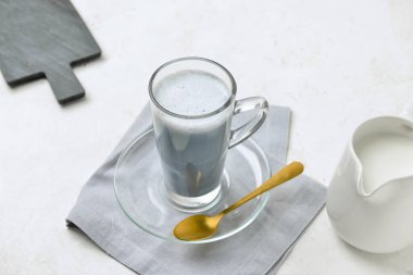 Bir bardak lezzetli mangal kömürü Latte, kaşık ve sütü ışık masasında.