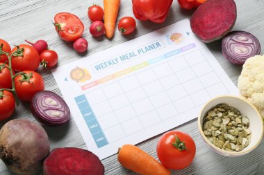 Haftalık yemek planlayıcısı ve gri ahşap arka planda farklı sağlıklı ürünler.