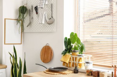 Mutfağın penceresinin yanında mutfak gereçleri ve ev bitkisi olan masa.