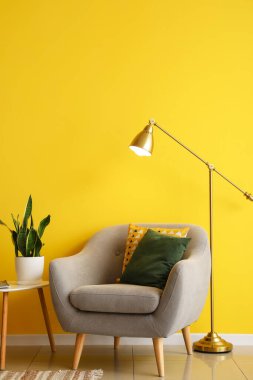 Sarı duvarın yanındaki koltuğu ve masası olan standart altın lamba.