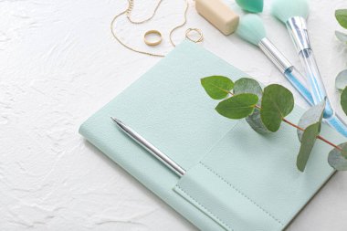 Okaliptüslü şık bir defter, beyaz arka planda makyaj fırçaları ve mücevherler, yakın plan