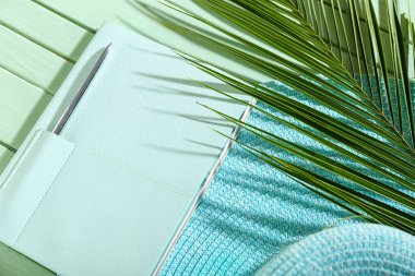 Yeşil ahşap zemin üzerinde kalem, şapka ve palmiye yaprağı olan şık bir defter, yakın plan.