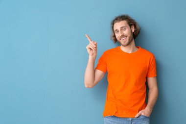 Şık tişörtlü yakışıklı genç adam mavi arka plandaki bir şeyi işaret ediyor.