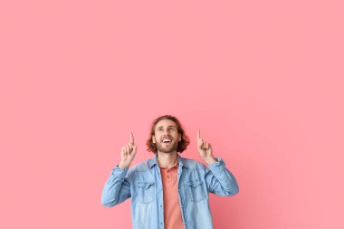 Pembe arka plandaki bir şeyi işaret eden şık elbiseli yakışıklı bir genç.