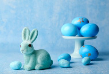 Mavi arka planda boyalı yumurtaları olan şirin Paskalya tavşanı.